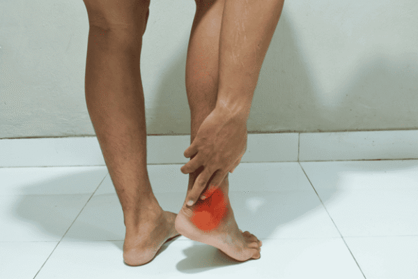 Person holding the back of the ankle where Achilles tendon pain is highlighted, illustrating shockwave therapy vs. physical therapy for Achilles tendonitis.